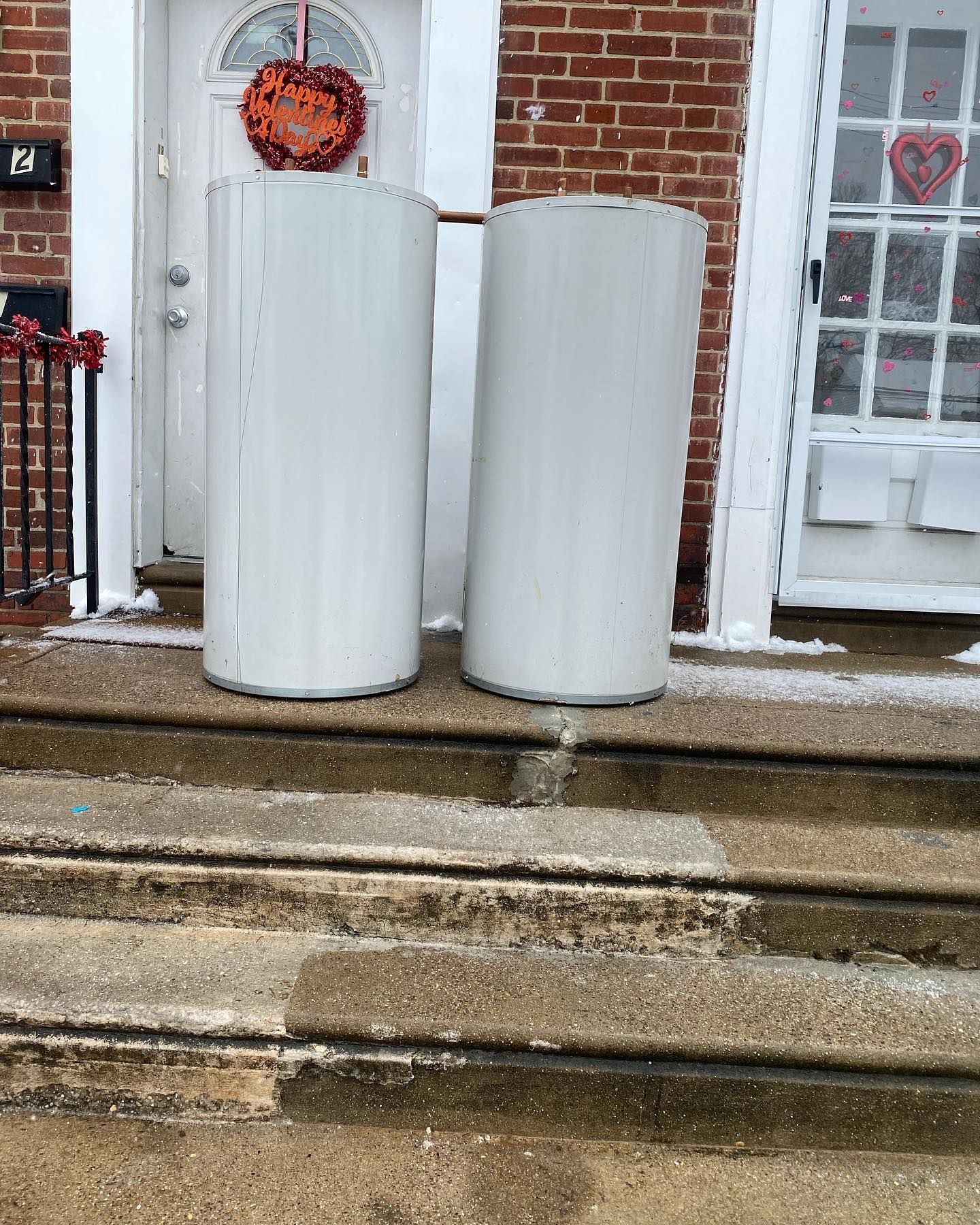 Two white cylindrical objects on steps in front of a building with a door and window.