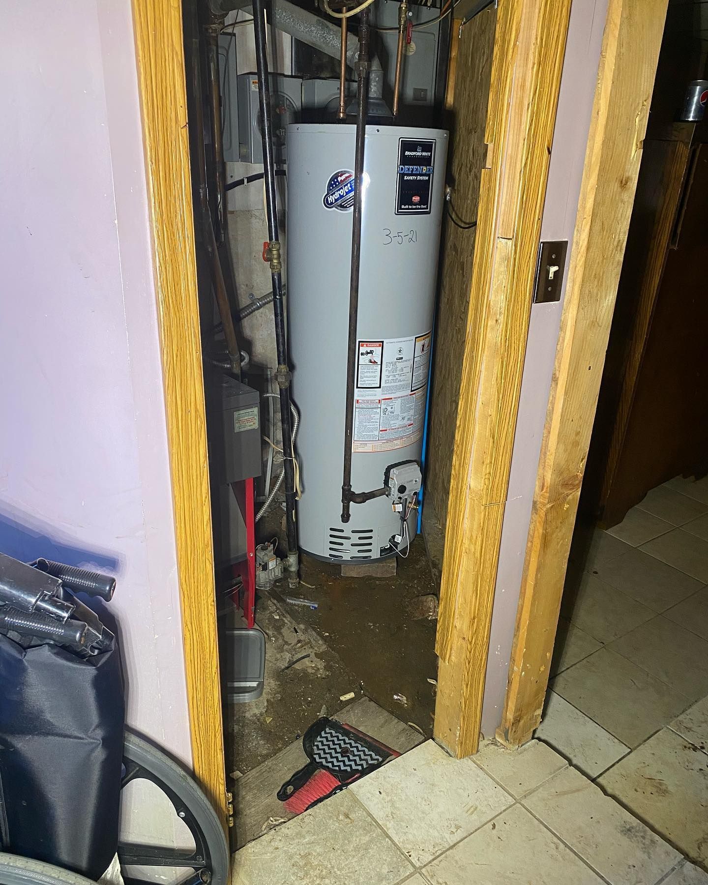 Water heater in a doorway, with water on the floor. Door frame is wood and pink walls.