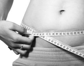 Hands measuring a waist with a tape measure, black-and-white close-up.