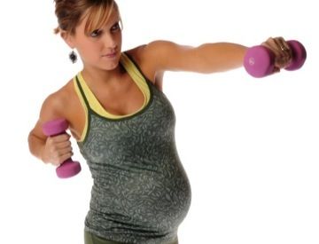 Pregnant woman exercising with pink dumbbells against a white background