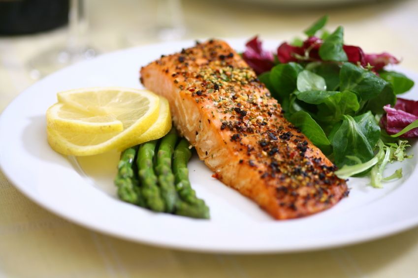Grilled salmon on a white plate with lemon wedges, asparagus, and mixed green salad