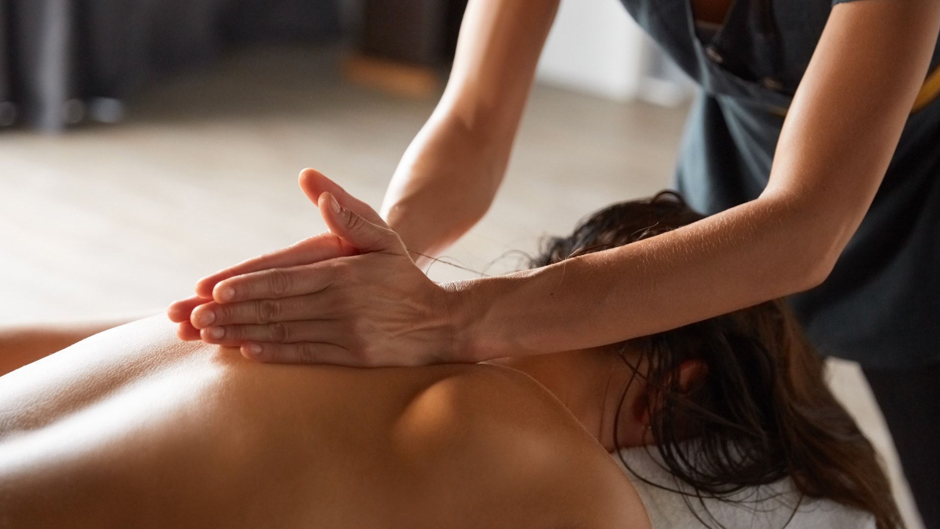 Massage therapist pressing shoulders and upper back on a person lying face down on a massage table