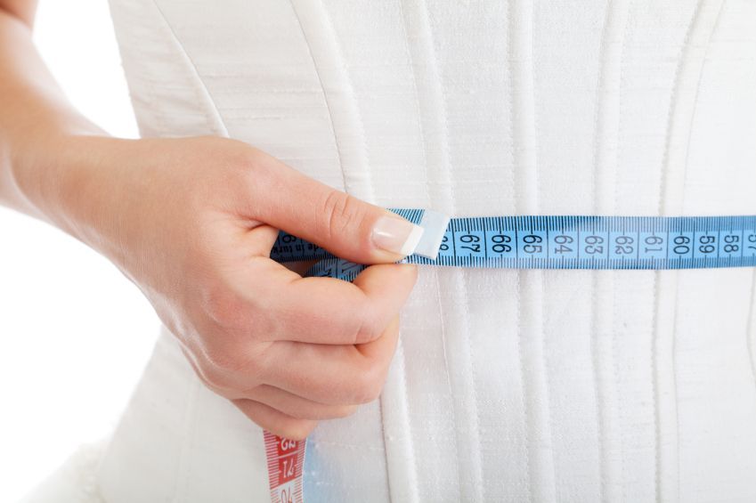 Hand holding a blue measuring tape around a white dress waist