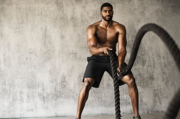 Athlete doing battle rope exercises in a gym against a gray wall.