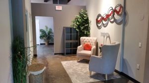 Modern office lobby with chairs, rug, wall art, and potted plants.