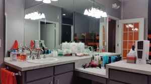 Bright bathroom vanity with large mirror, countertop cluttered with toiletries and a hair dryer.