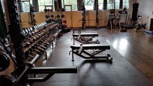 Gym interior with dumbbell rack, benches, and exercise equipment on a rubber floor