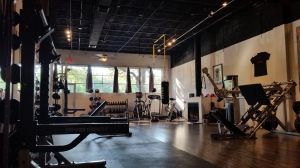 Empty gym interior with weight machines, benches, and large windows letting in daylight