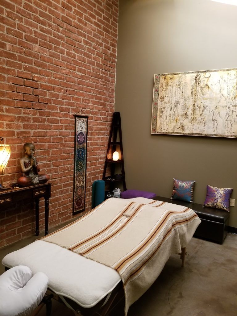 Modern massage room with brick wall, treatment table, floor lamp, and framed abstract art