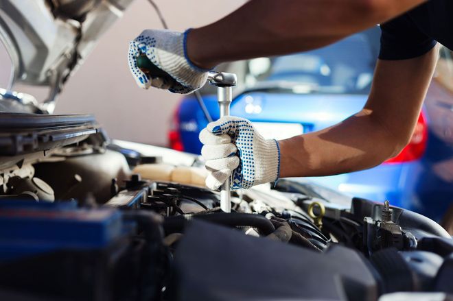 Mechanic tightening a car engine bolt with a wrench in a garage, wearing gloves.