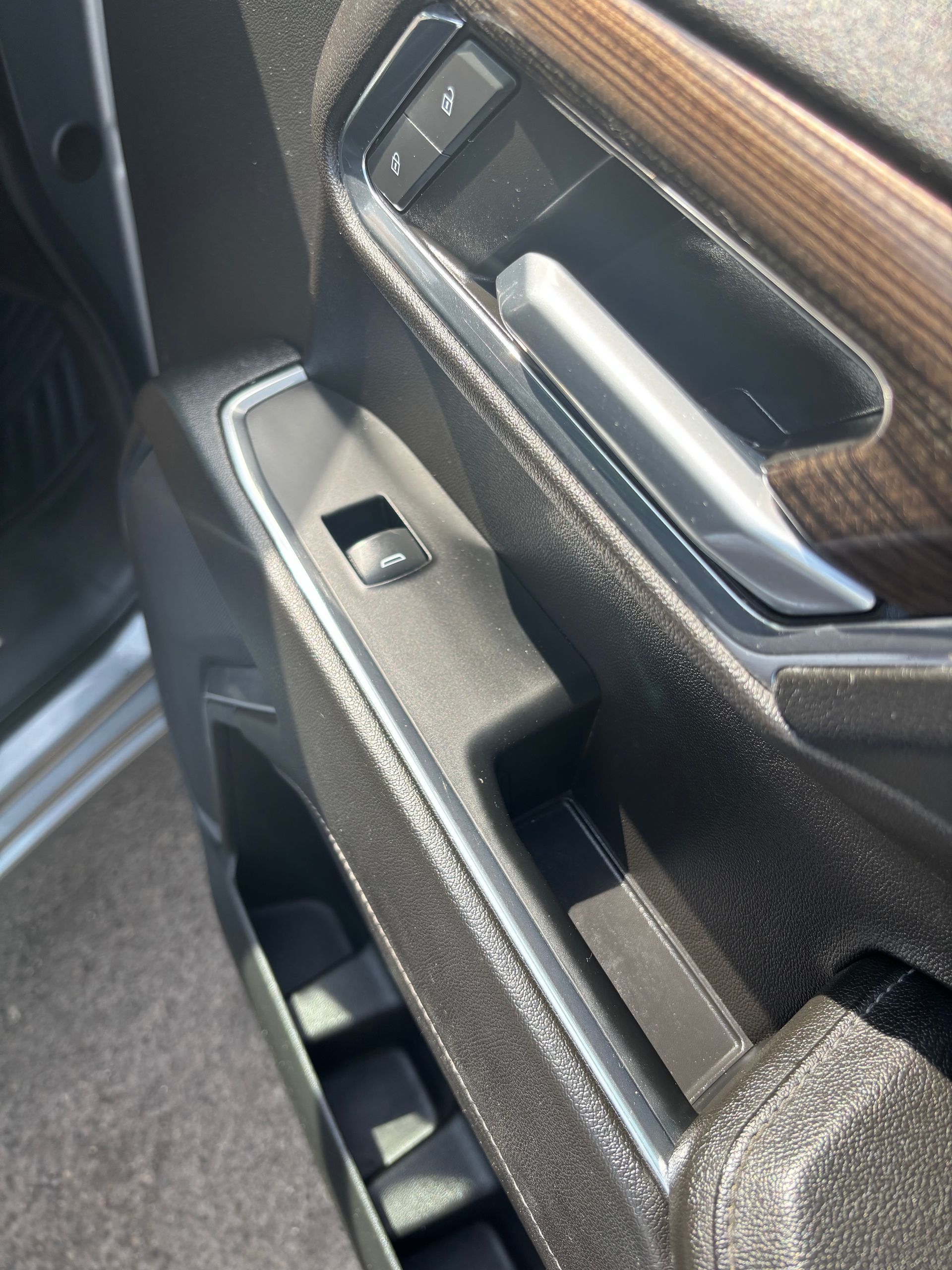 Close-up of a car door interior with black trim, silver handle, and wood accent panel