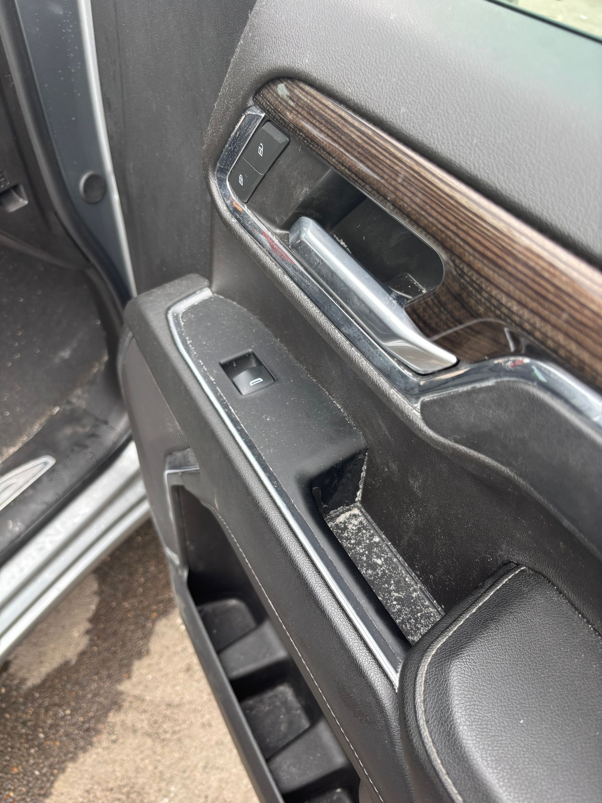 Car door interior with black trim, wood accent, chrome handle, and window controls close-up