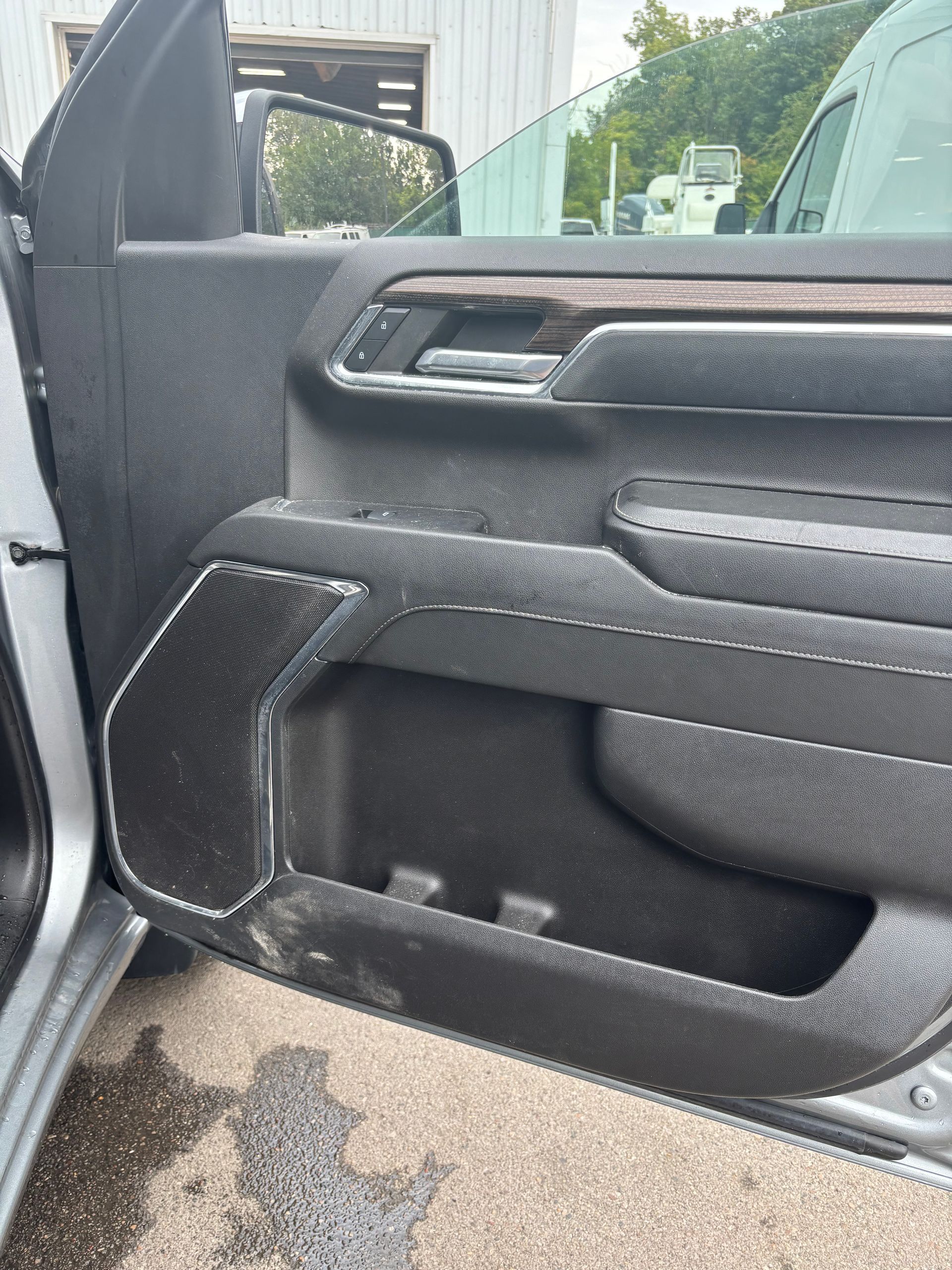 Open car door with black interior panel and speaker, showing the outside pavement and street.