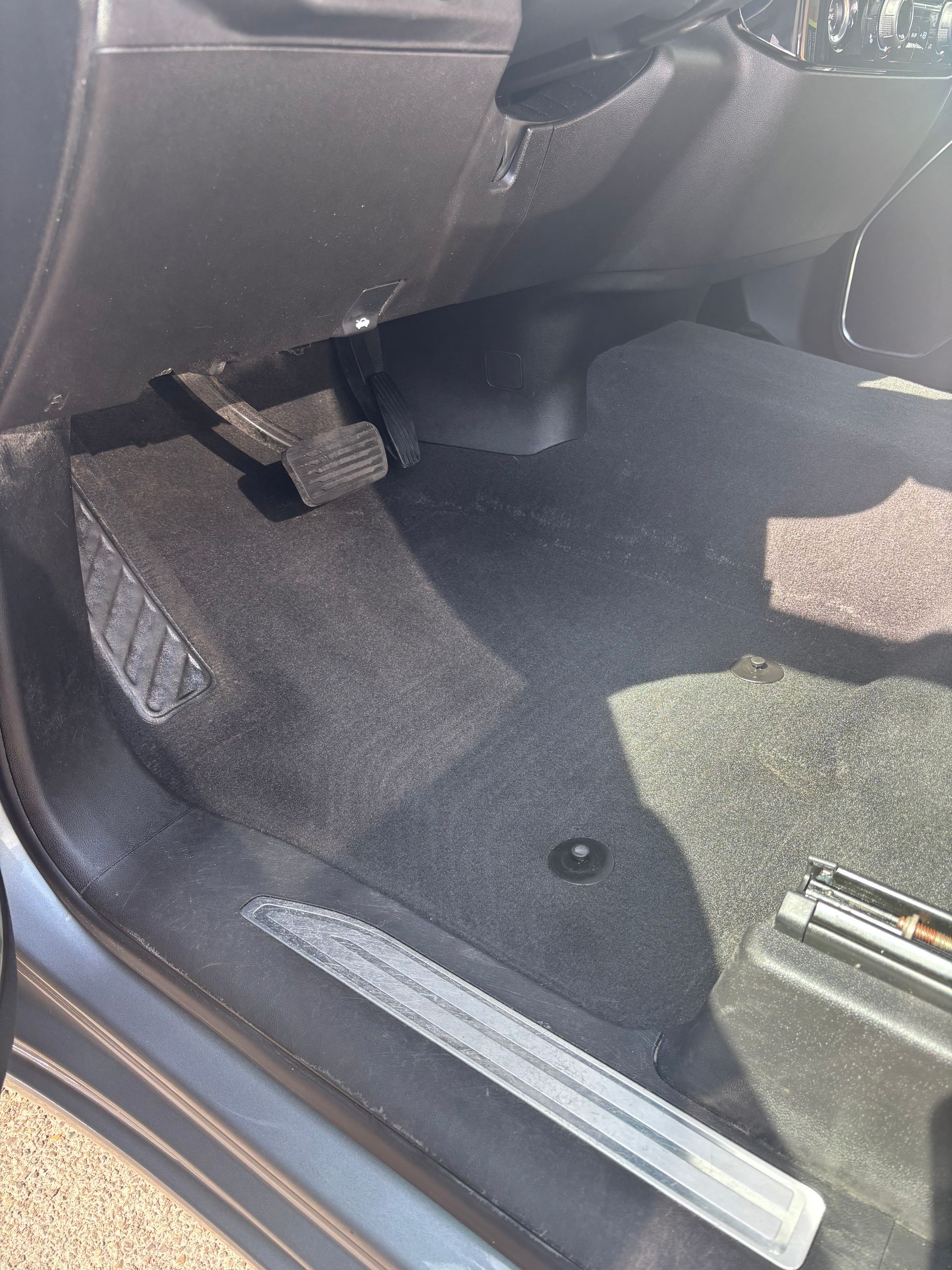 Car interior footwell with black carpet and a silver door sill trim, seen from the open door.