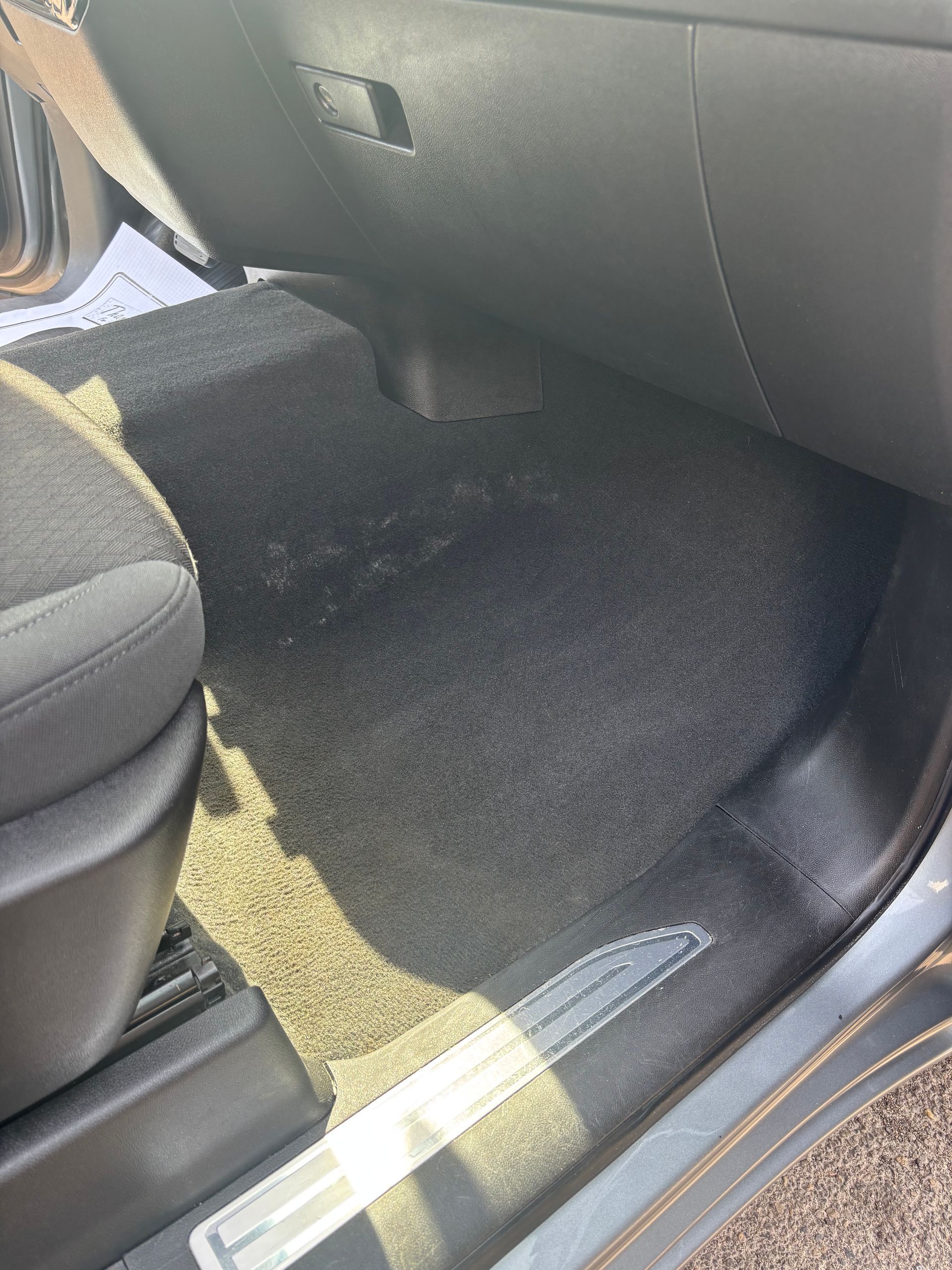 Car floor with black carpeted mats and dark seat base near the door sill