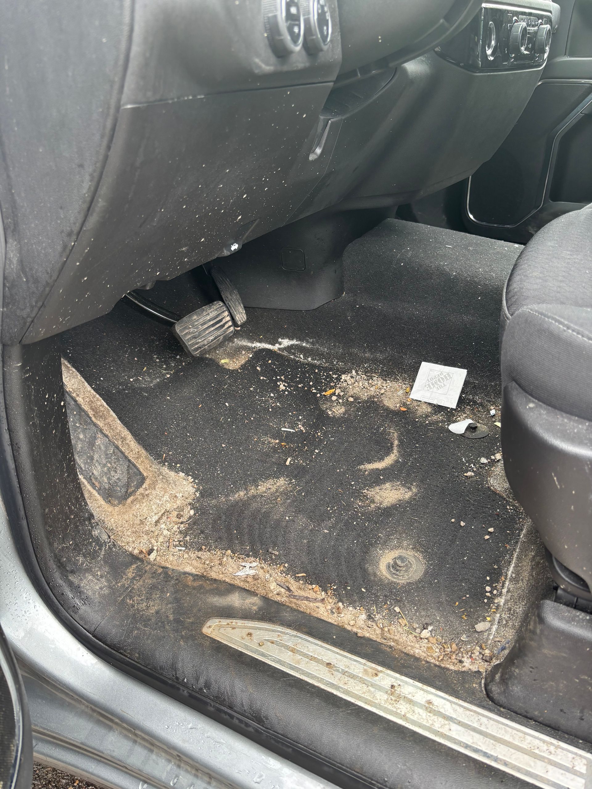 Car interior floor mat covered with dirt and debris, seen from the open rear door