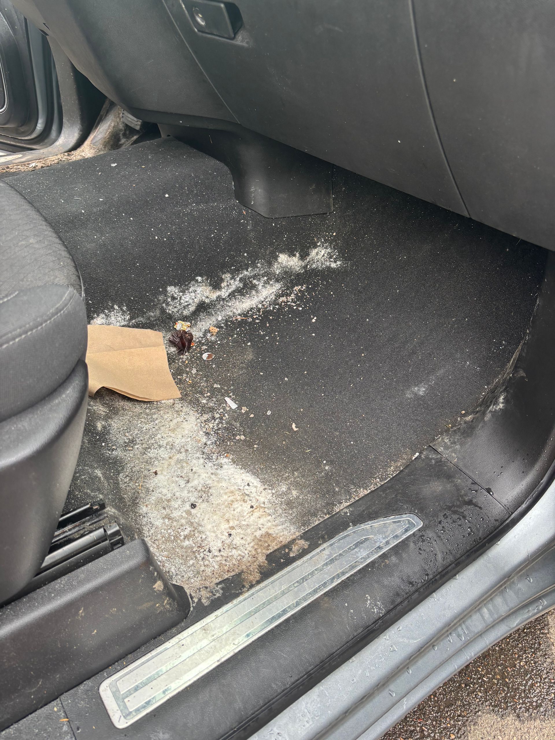 Car floor with white powdery spill and cardboard near the front passenger seat