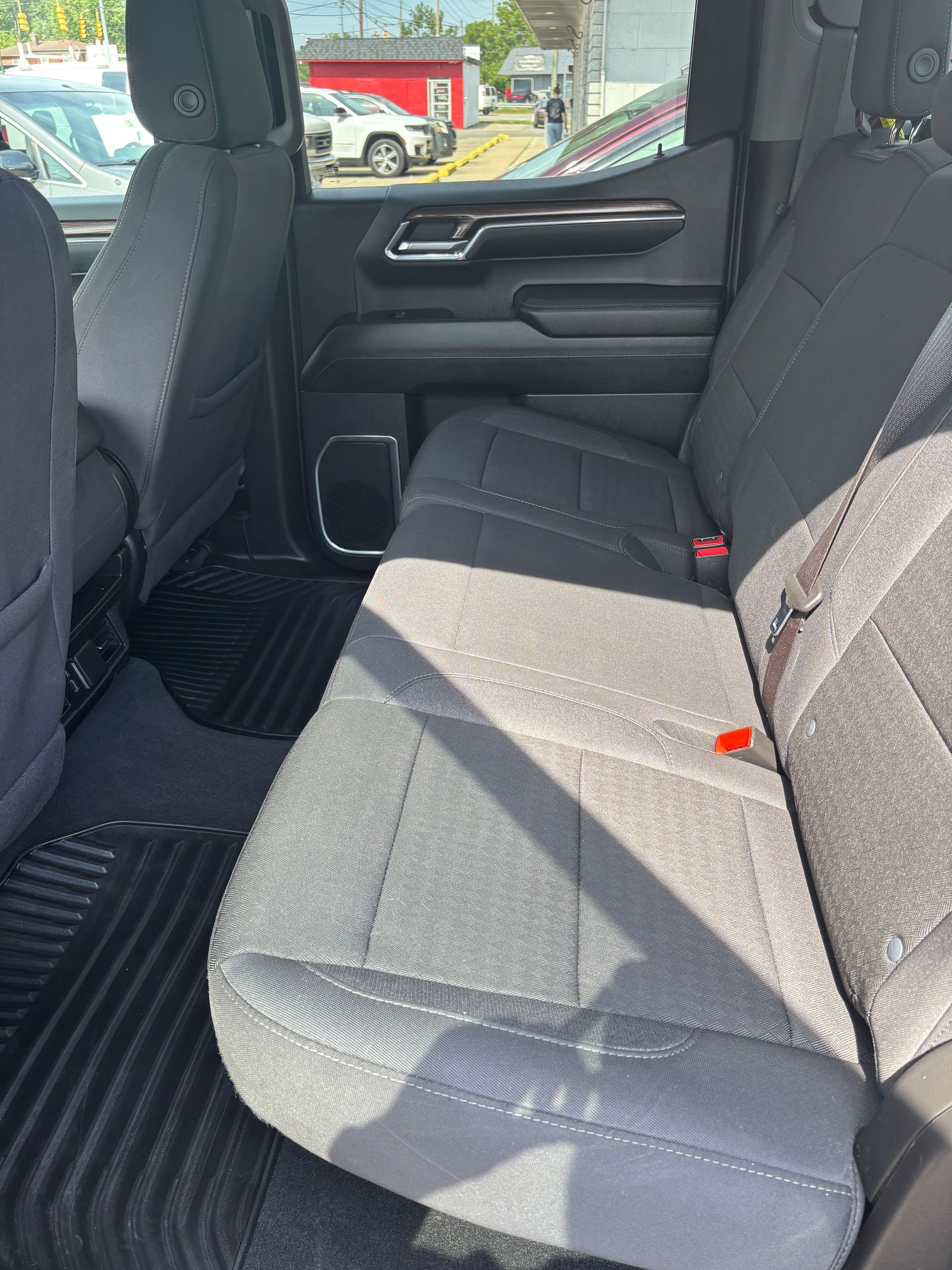 Back seat of a vehicle with gray fabric seats and floor mats, viewed from the open door