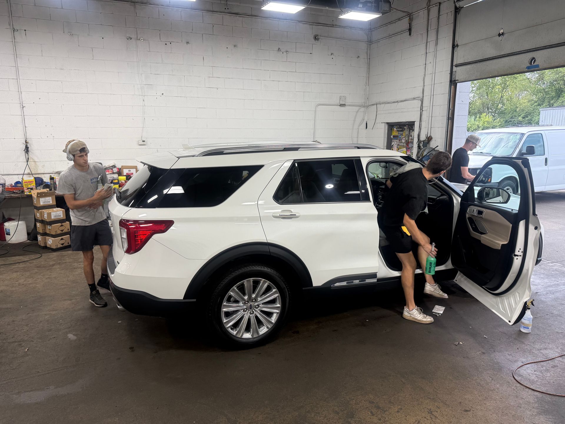 White SUV in a garage with people standing by the open doors during what appears to be service or inspection.