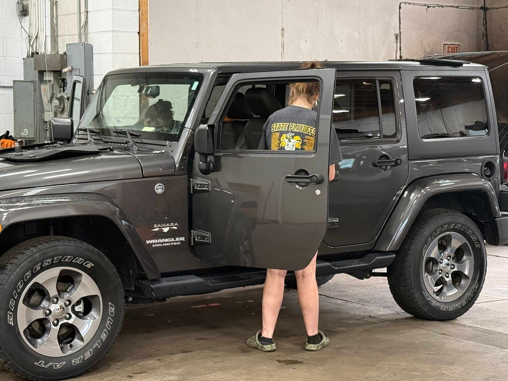 Person standing by an open door of a black Jeep in a garage.