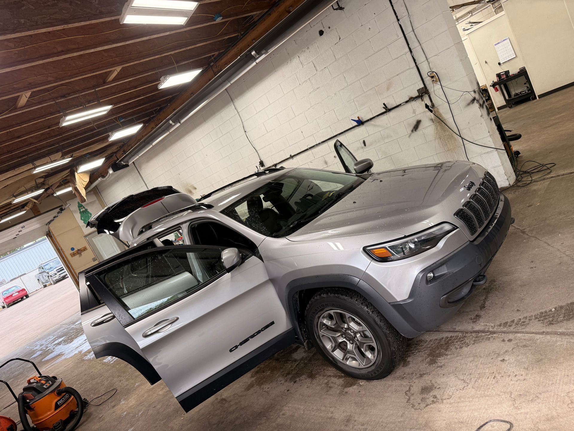 Silver SUV inside a warehouse-like garage with its driver door open and hood raised