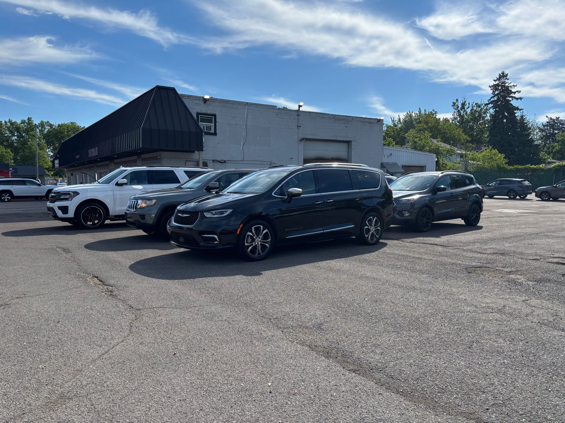 Parking lot with several parked cars beside a low white building under a clear sky