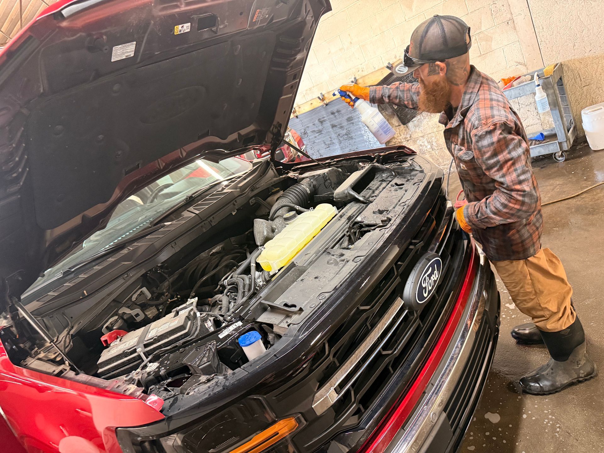 Mechanic inspecting a red car with hood open in a garage