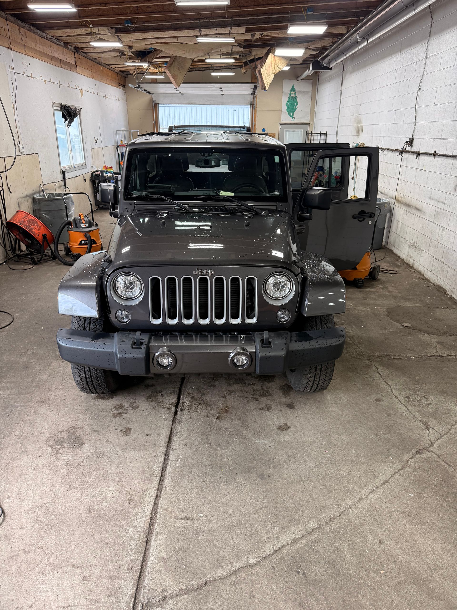 Black Jeep Wrangler in a garage with its driver door open.