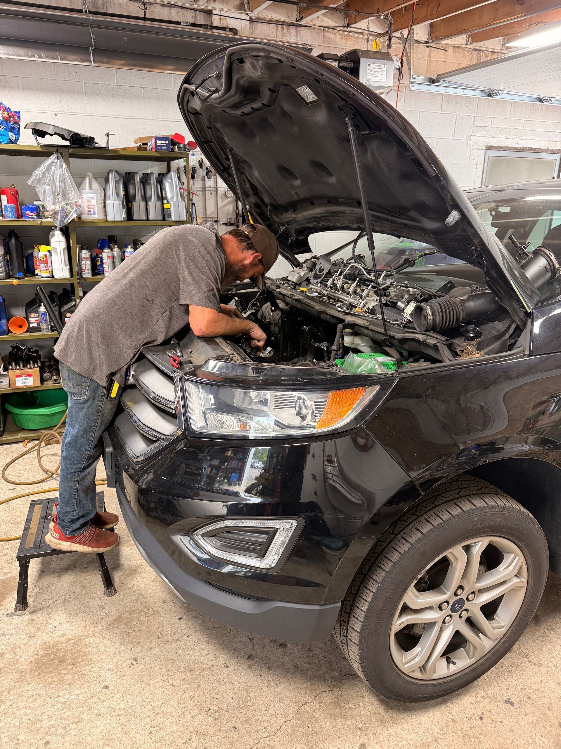 Mechanic inspecting a black SUV with the hood open in a garage