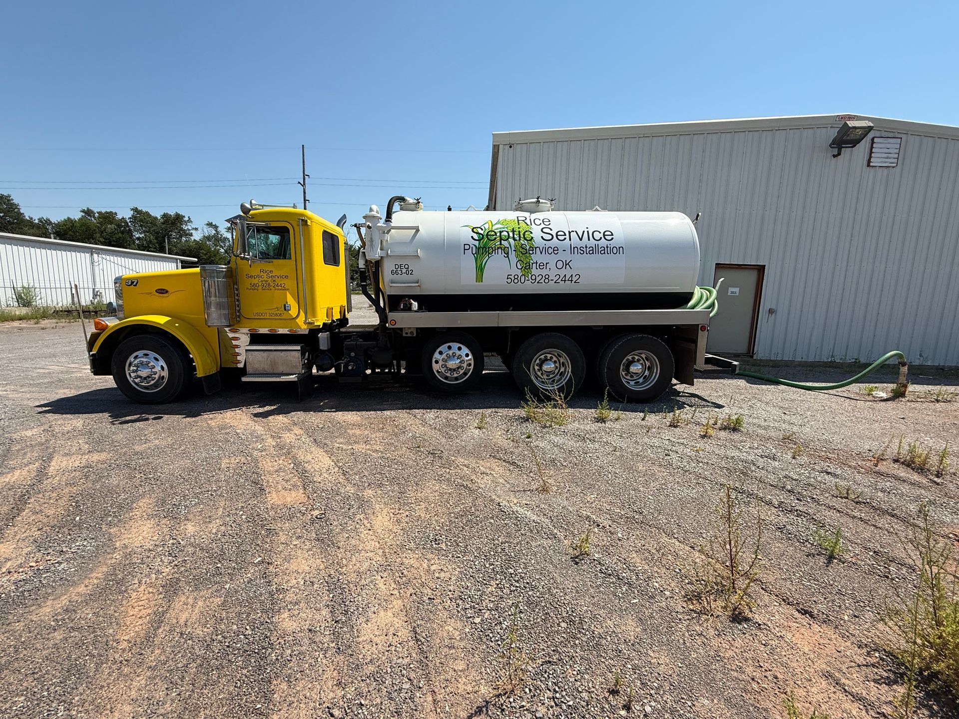 Yellow septic truck parked in front of a white building on gravel.