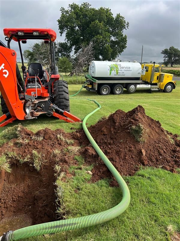 A tractor, septic truck, and hose draining a hole in the ground on a green lawn.