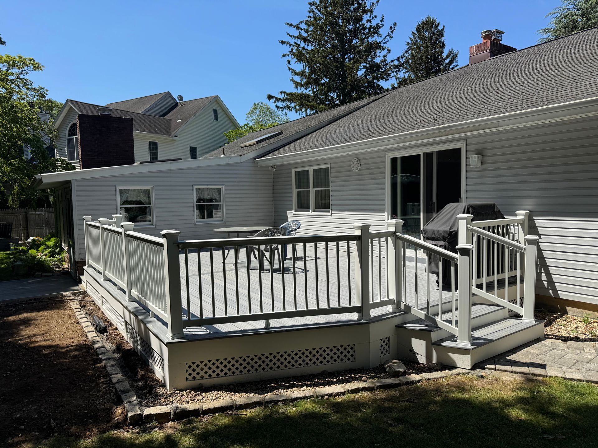 A gray wooden deck with a railing is attached to a light gray house on a sunny day.