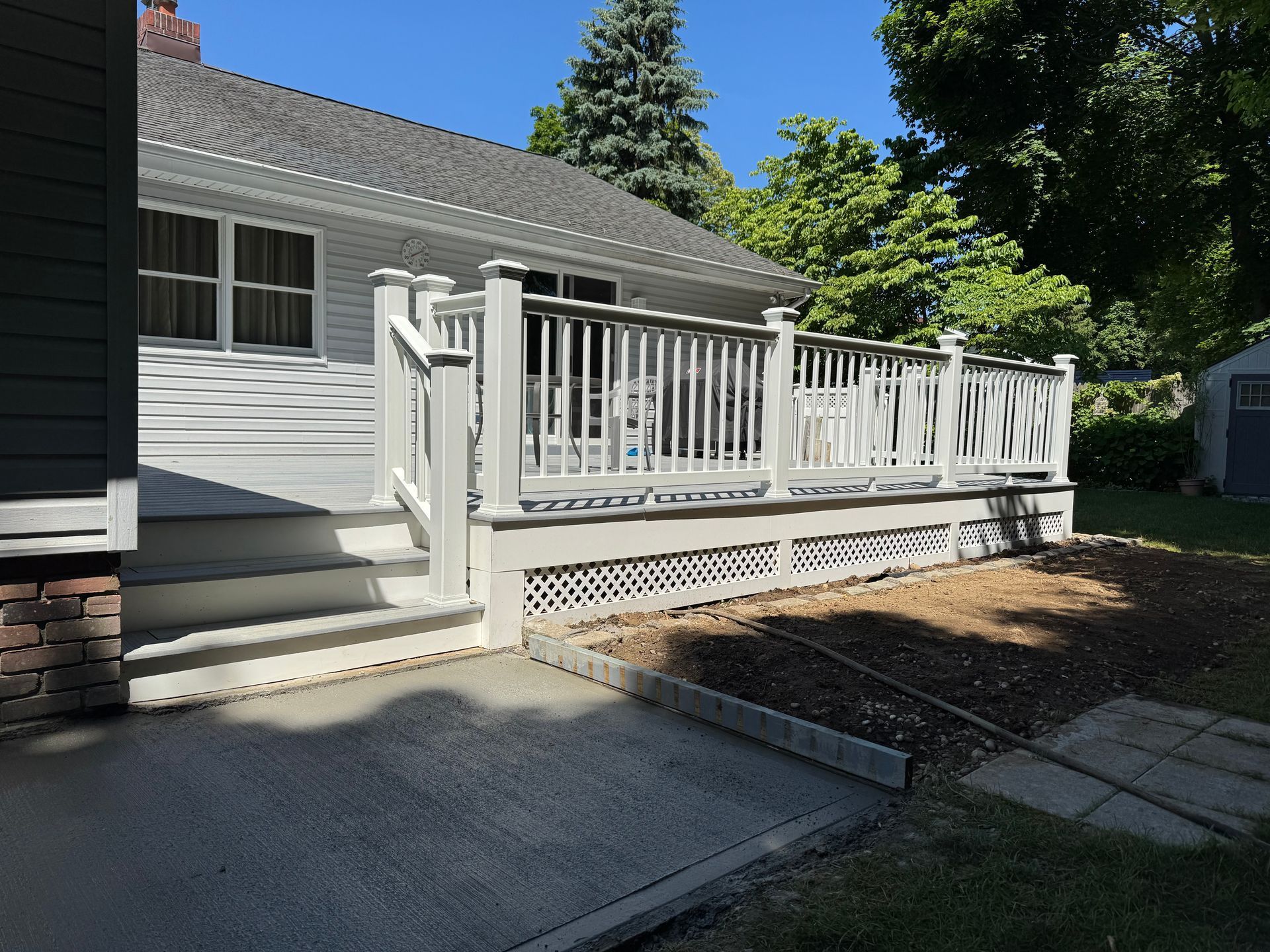 White deck attached to a house, with concrete pathway and landscaping.