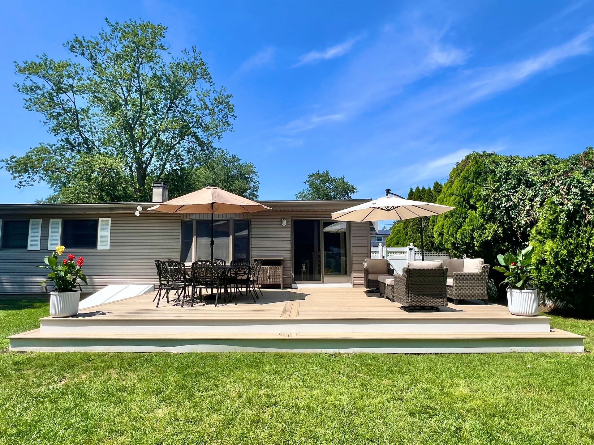 Back deck with patio furniture, umbrellas, and potted plants on a sunny day.