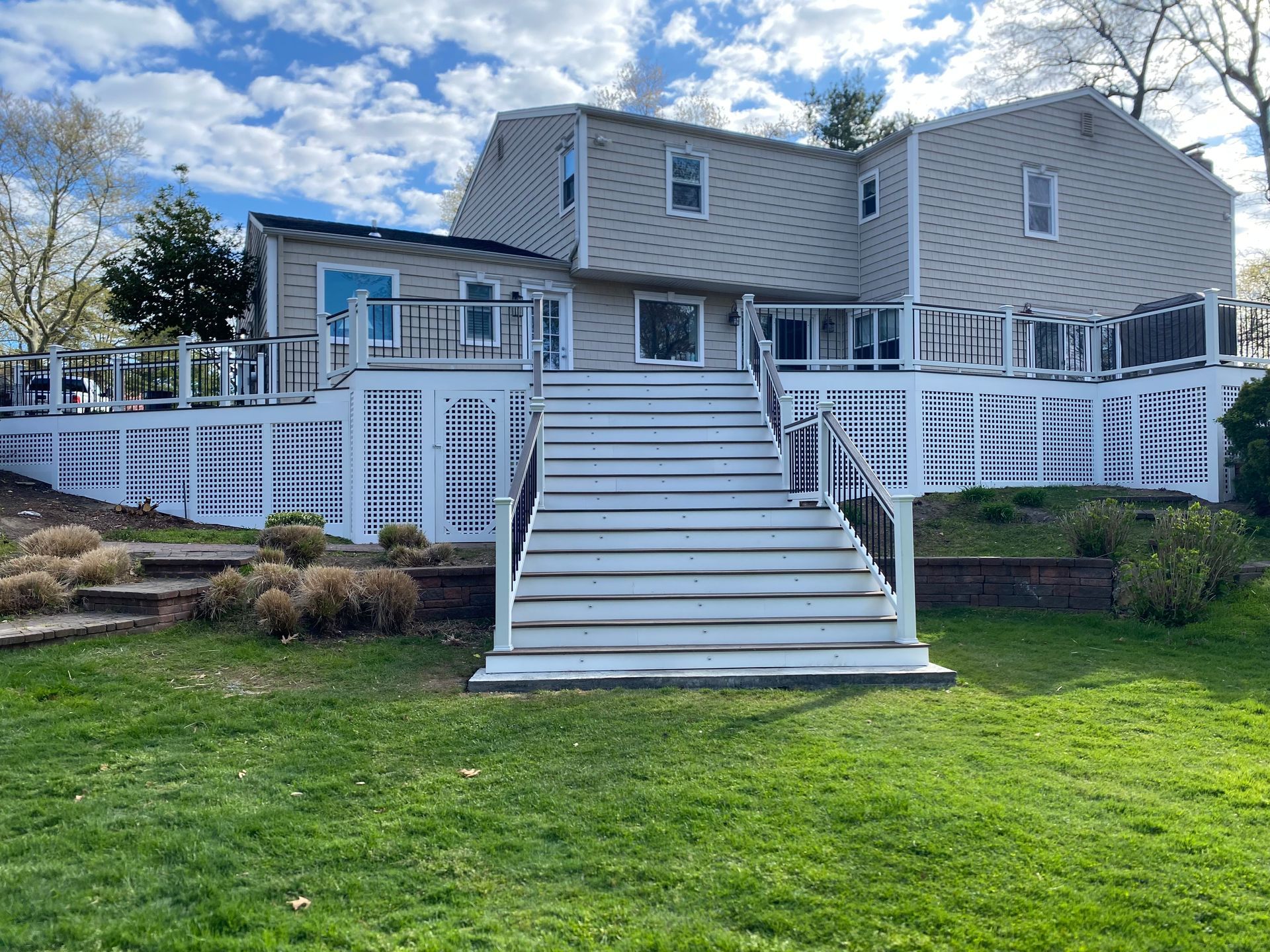 A two-story house with a large deck, stairs, and a grassy yard under a cloudy sky.