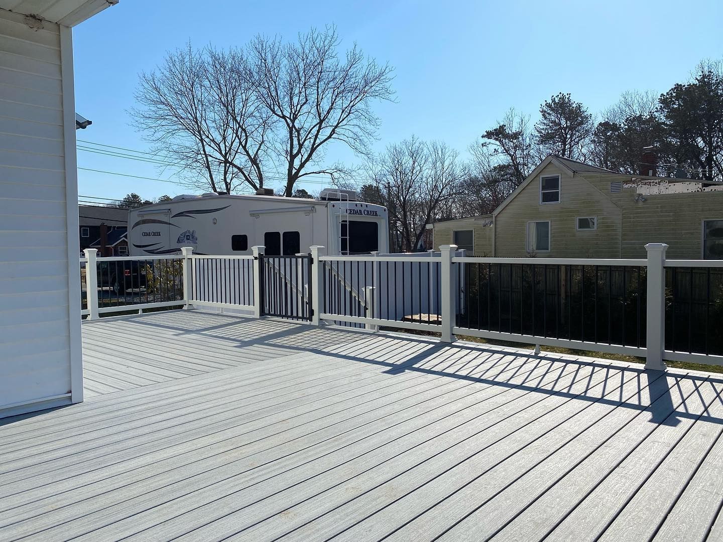 A white deck with a white railing and a white trailer in the background.