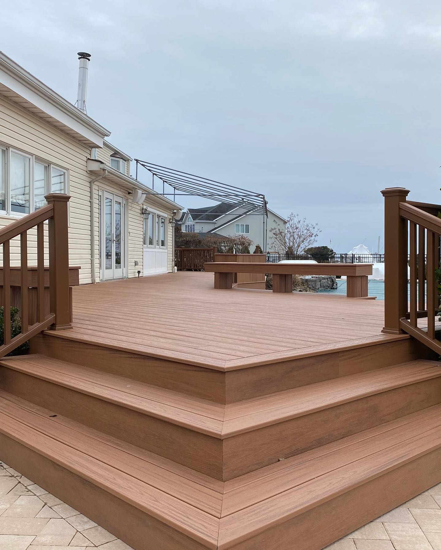 A large wooden deck with stairs and benches in front of a house.