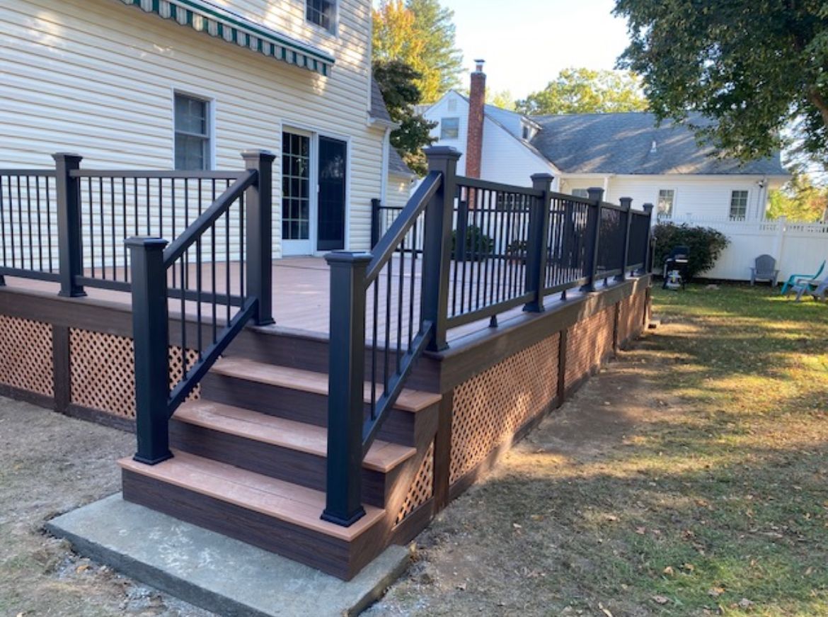 A deck with stairs and a black railing in front of a house.