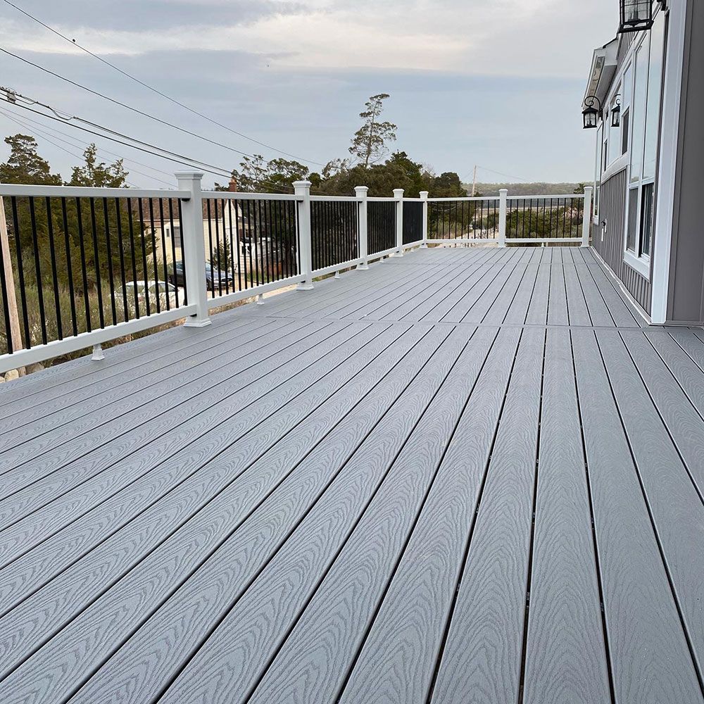 A large gray deck with a white railing and a house in the background.