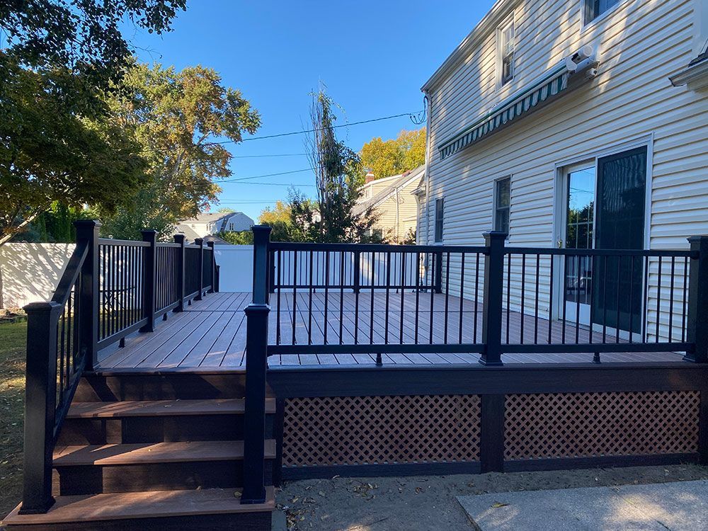 A large wooden deck with stairs and a black railing in front of a white house.