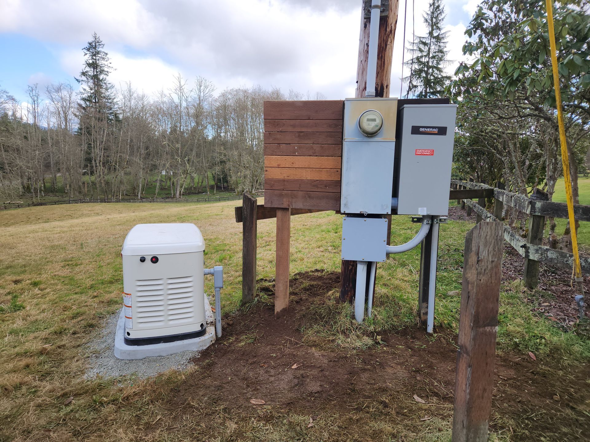 Generator beside a utility pole with electrical boxes in a grassy field.