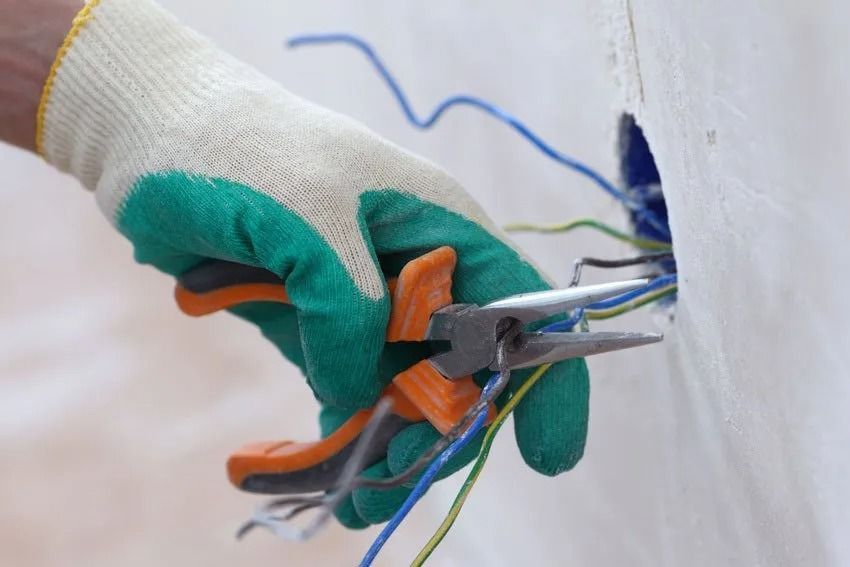 Hand in green and white work glove using pliers to work with wires in an electrical box.