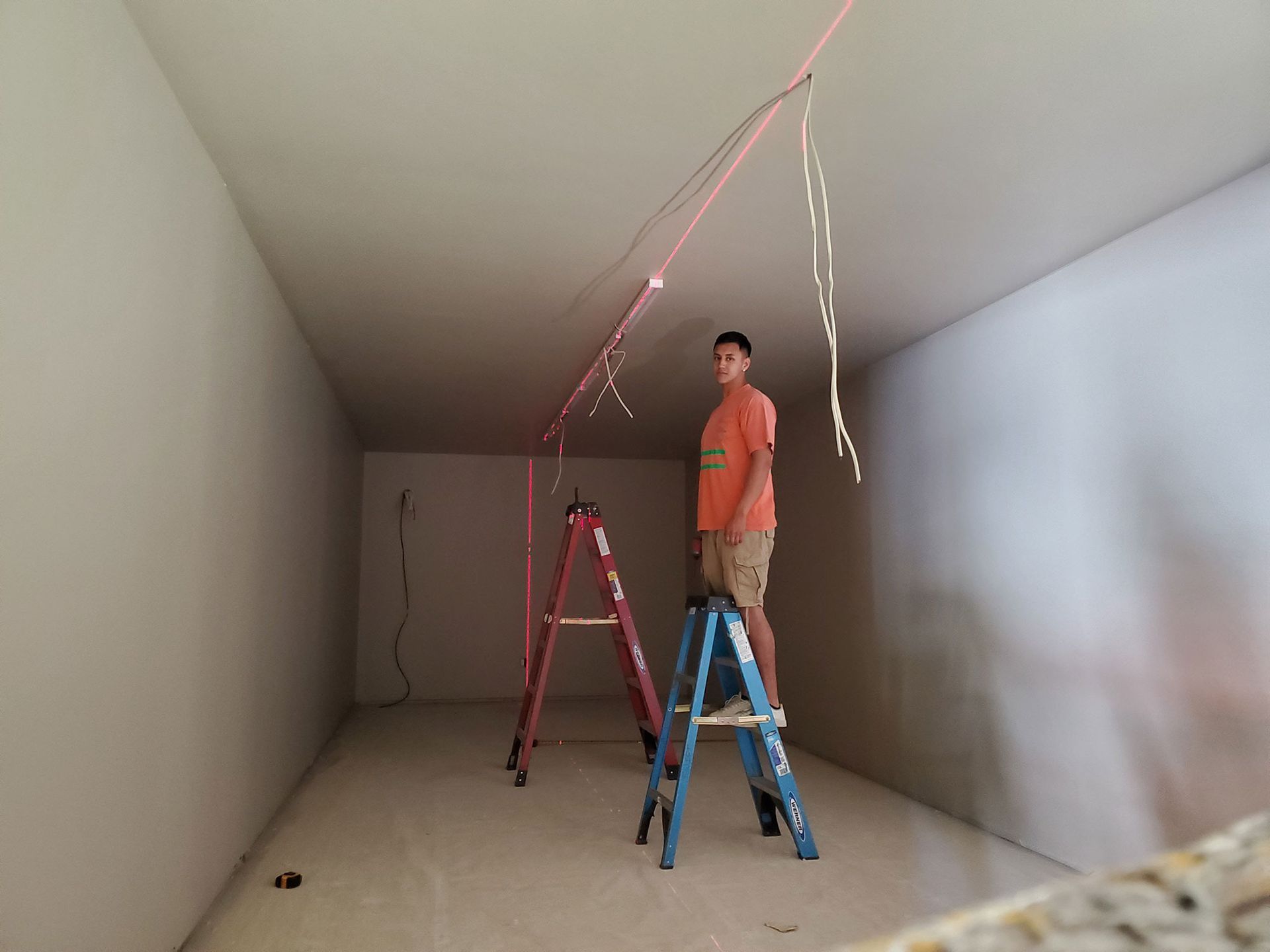 Man on a blue ladder installs lights in a room with two other ladders.