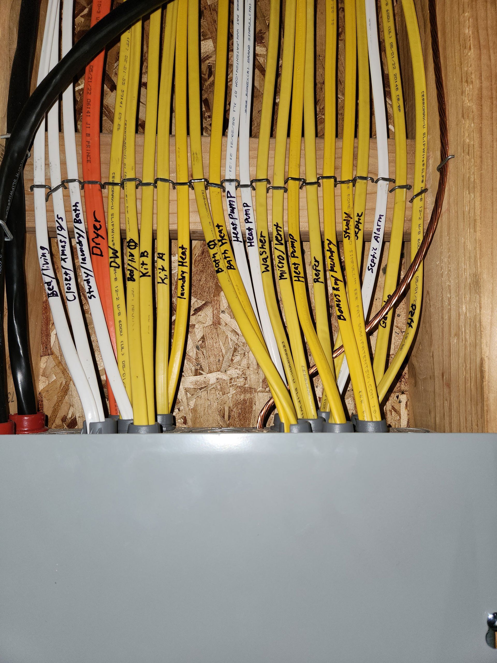Electrical wires labeled with markers emerge from a gray panel, mounted on a wooden surface.