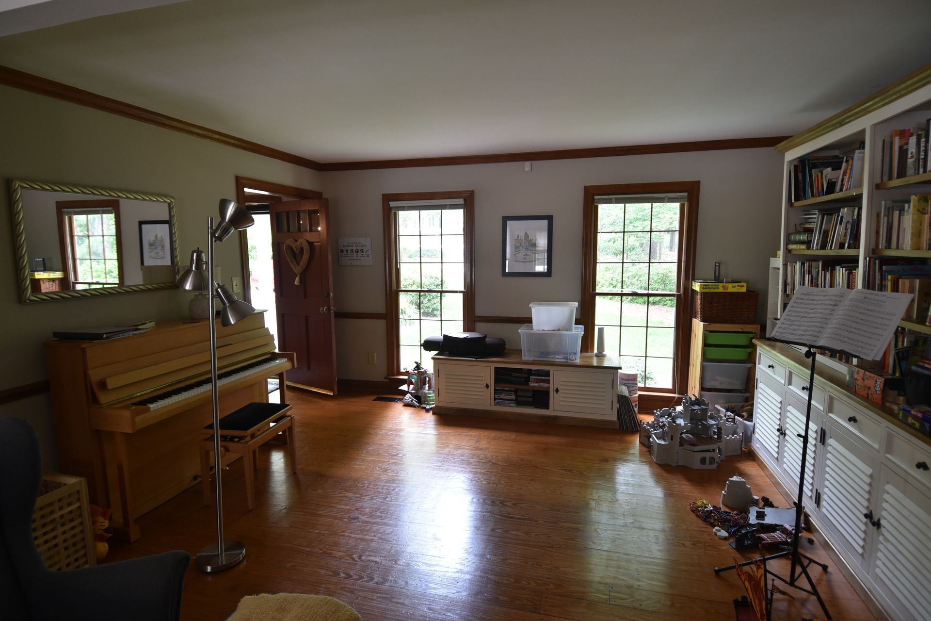 Living room with piano, bookshelves, and windows. Brown trim, light-colored walls and floor.