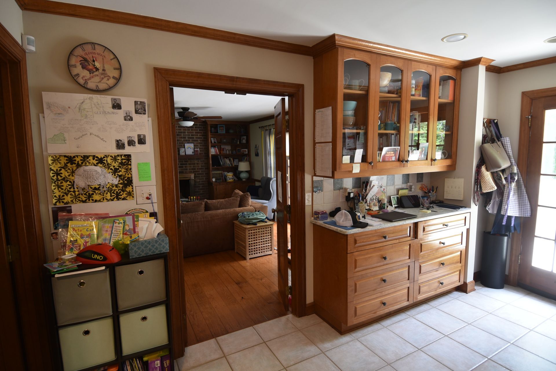 Kitchen with wooden cabinets, open doorway to a living room, and a small storage unit.