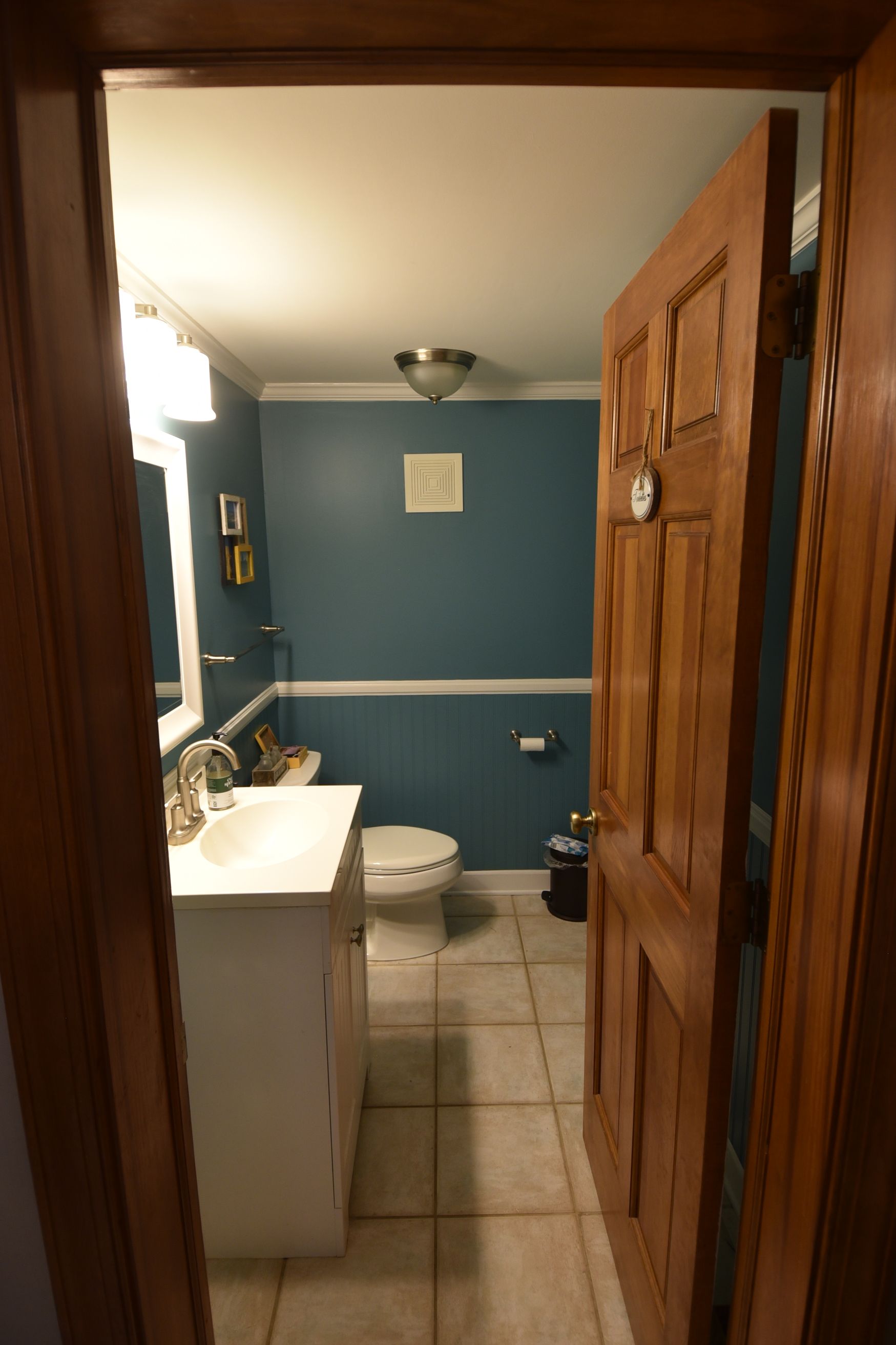Bathroom interior: white vanity, toilet, teal walls, wood door open from a doorway.