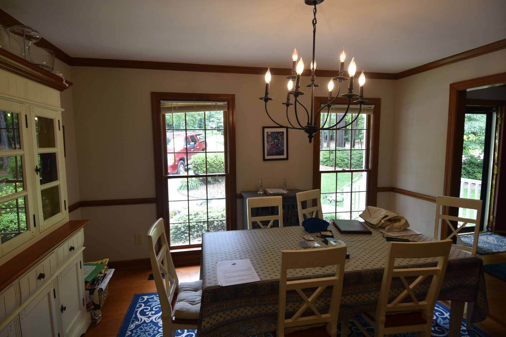 Dining room with table set for a meal, a chandelier, windows, hutch, and chairs.