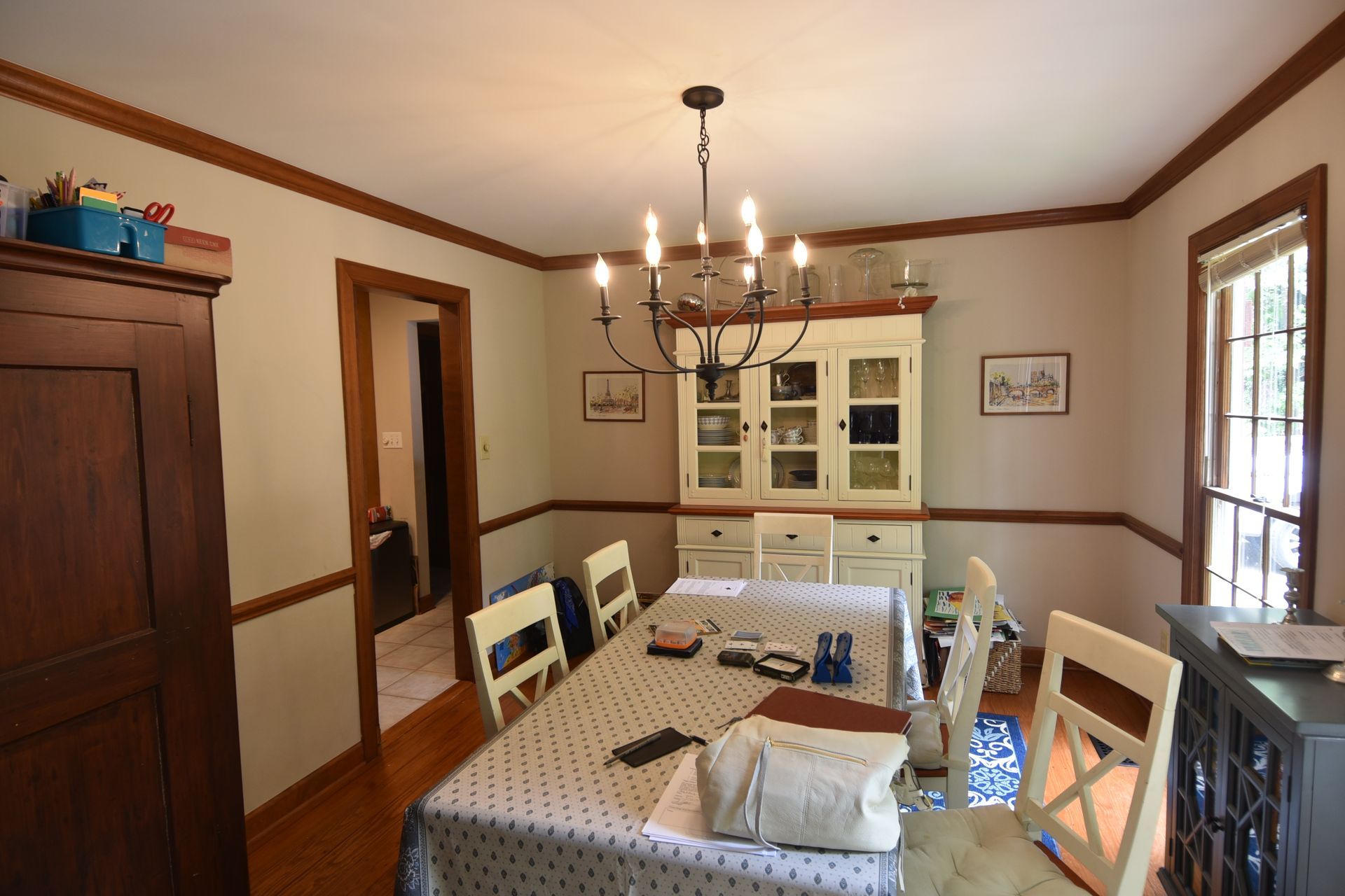 Dining room with chandelier, long table with chairs, and a cabinet.
