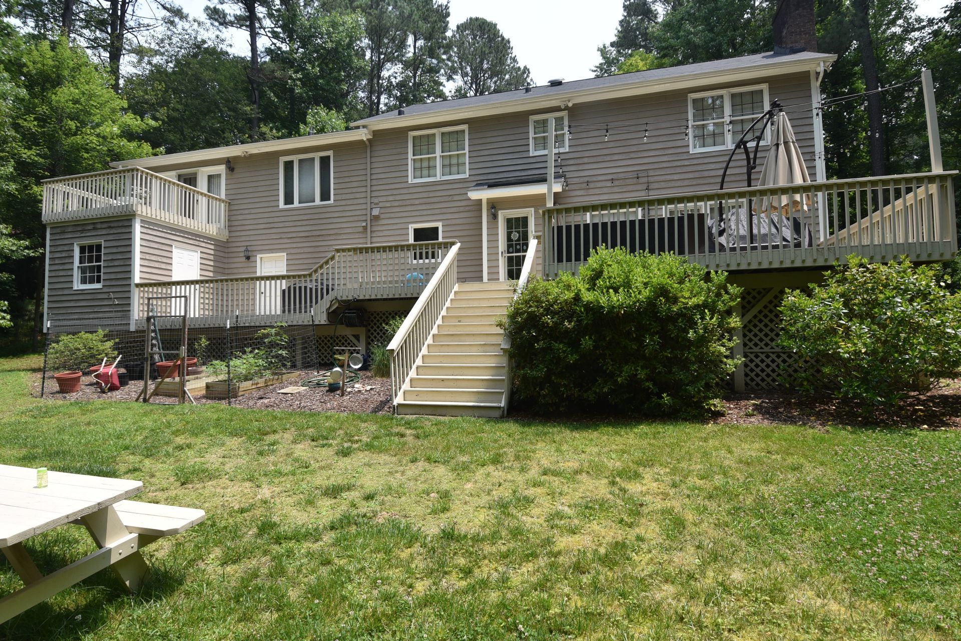 Back of a two-story house with a large wooden deck and steps leading to a grassy backyard.